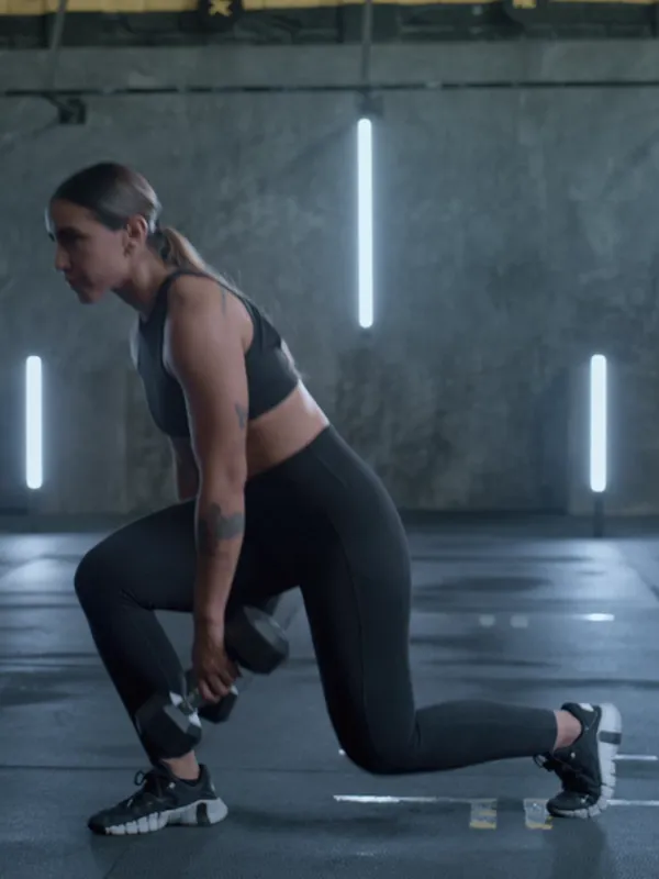 A woman in a deep lunge holding dumbbells